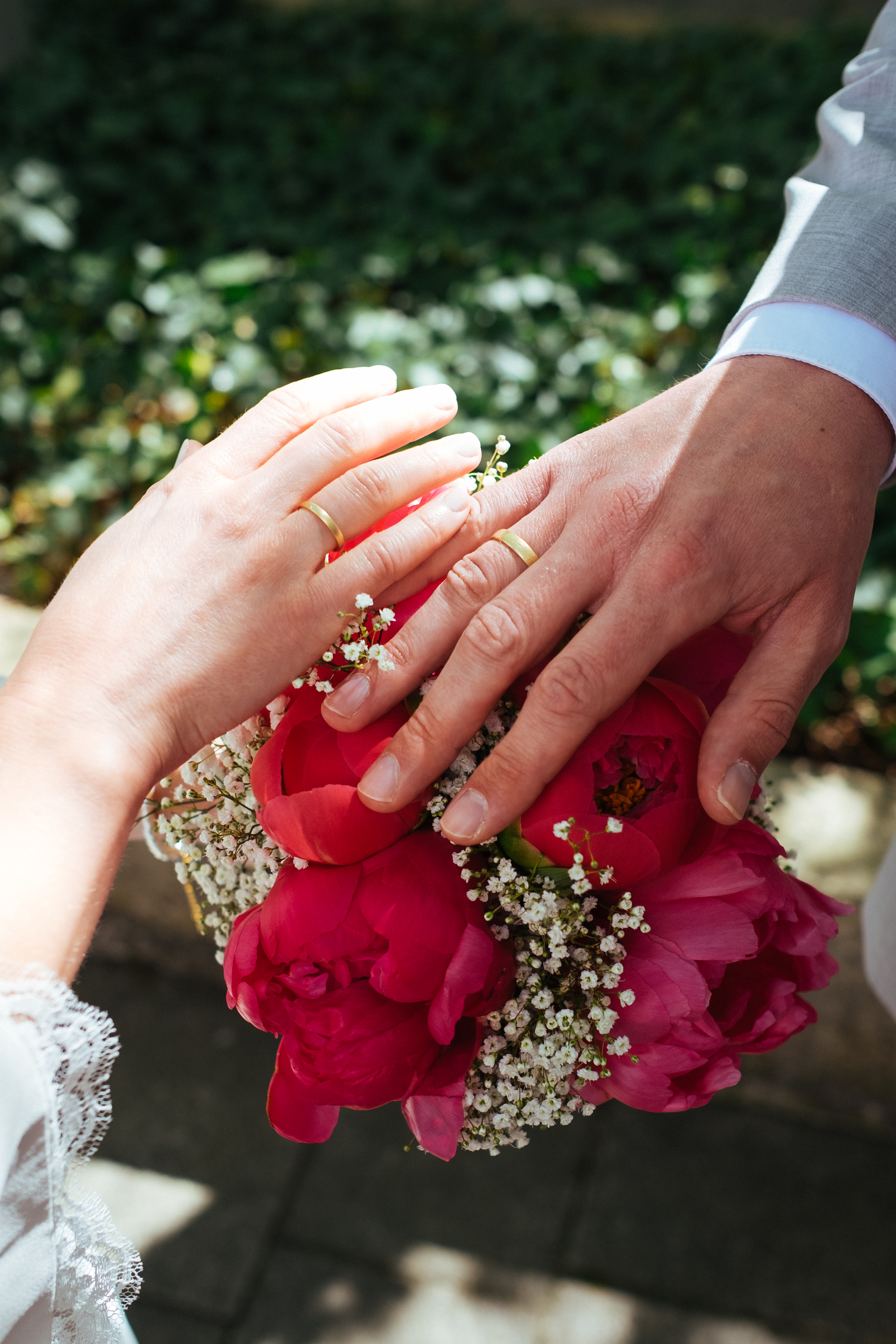 Hände des Brautpaares mit Eheringen vor dem Brautstrauß