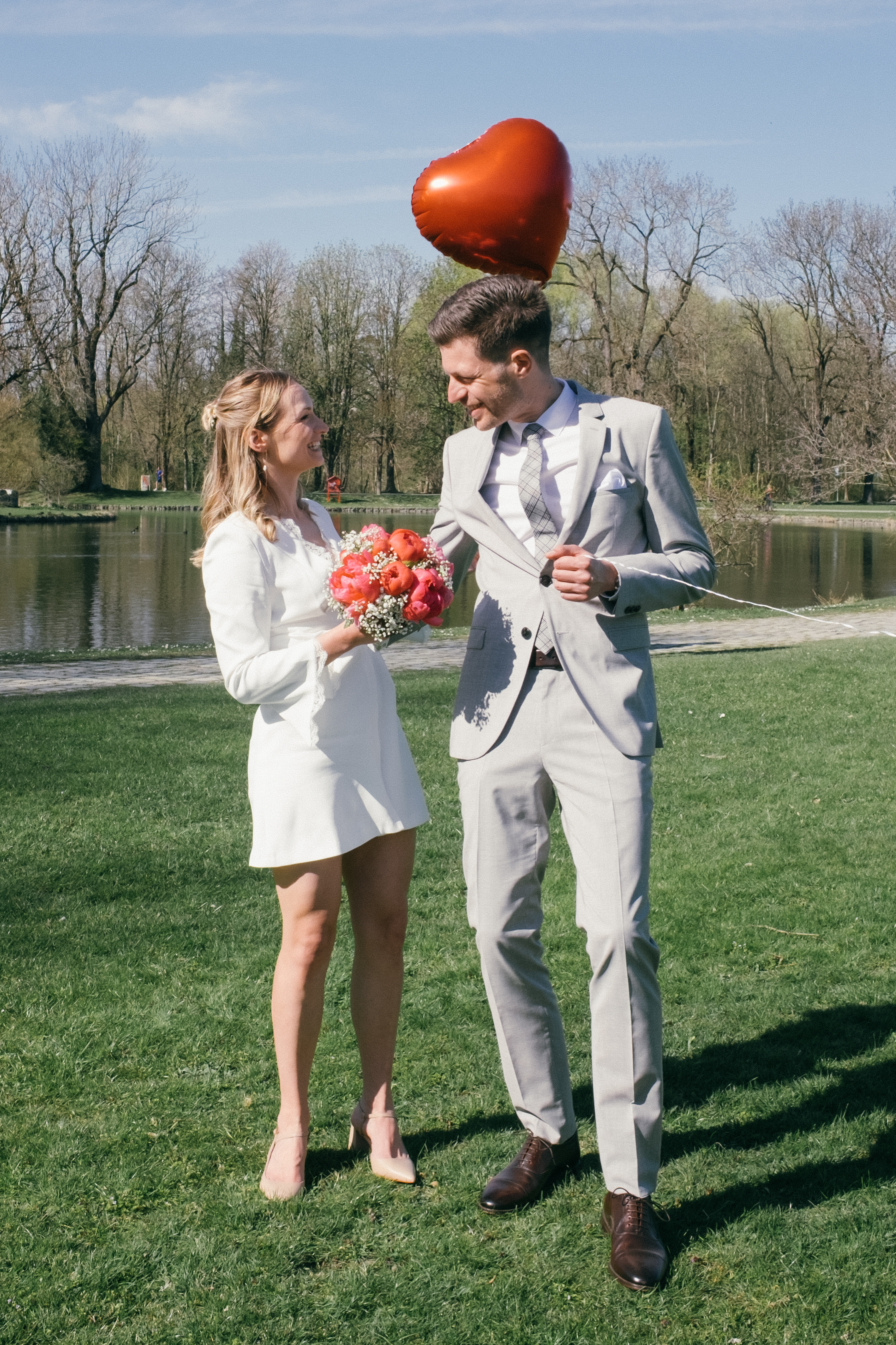 Glückliches Brautpaar nach Trauung im Park mit einem Herzluftballon in der Hand