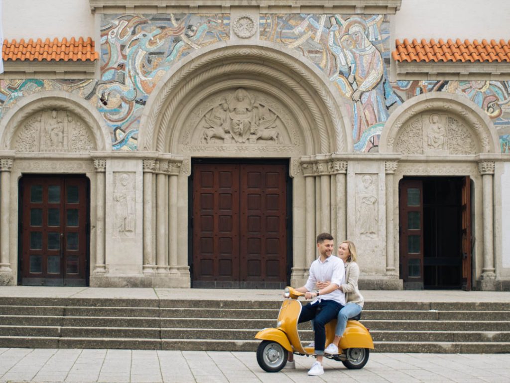 Lachendes Paar auf einer Vespa vor einer Kirche