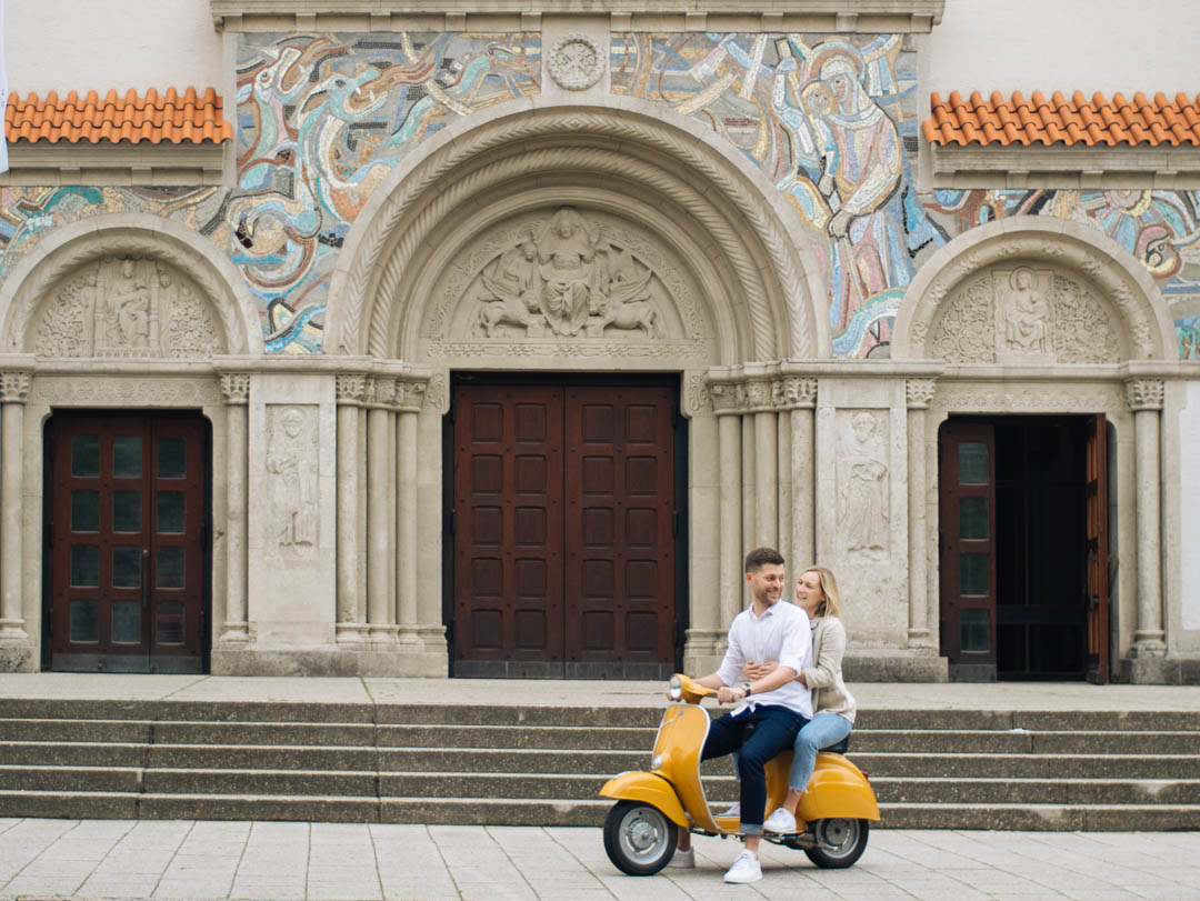 Lachendes Paar auf einer Vespa vor einer Kirche