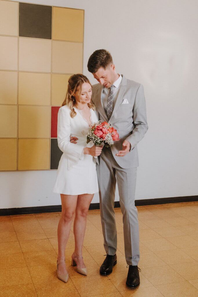 Das Brautpaar wartet auf ihren Termin für ihre stadesamtliche Trauung und schauen auf den Brautstrauß