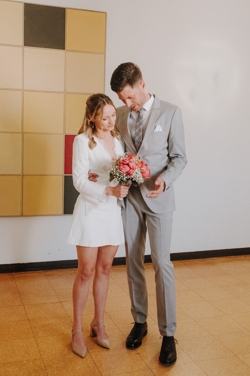 Das Brautpaar wartet auf ihren Termin für ihre stadesamtliche Trauung und schauen auf den Brautstrauß