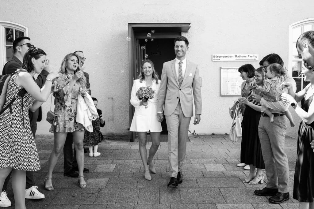 Brautpaar läuft nach Trauung aus dem Standesamt durch ihre jubelnde Gäste und Familien