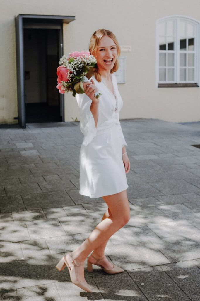 Eine lachende Braut steht mit ihrem Brautstrauß vor dem Standesamt nach der Hochzeit