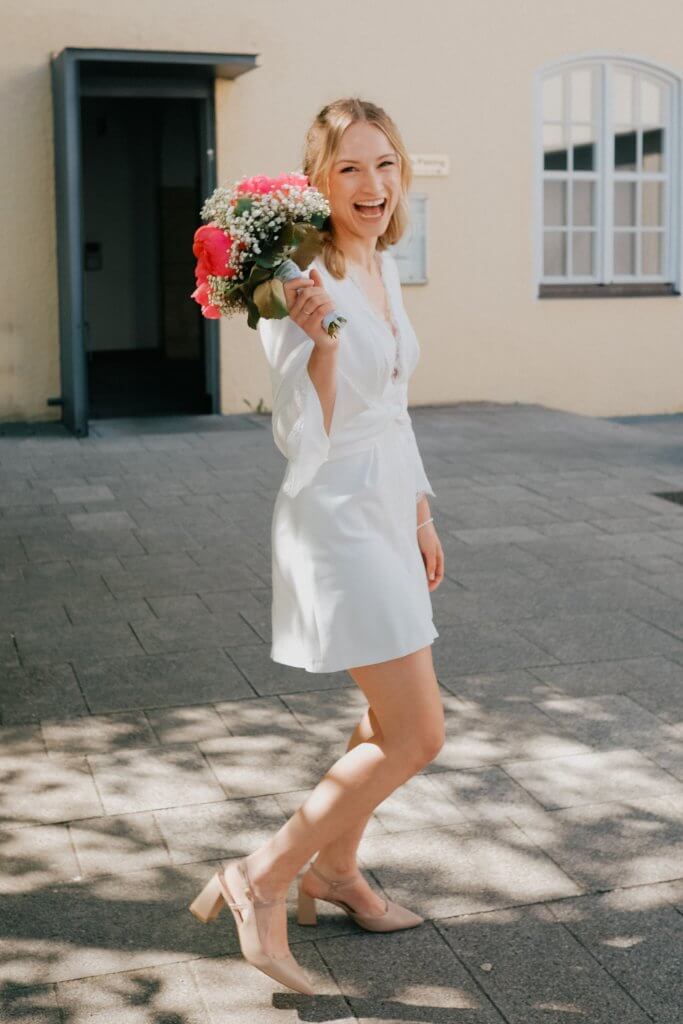 Eine lachende Braut steht mit ihrem Brautstrauß vor dem Standesamt nach der Hochzeit